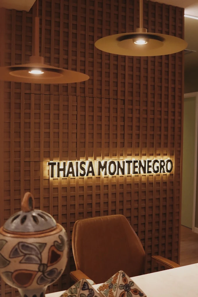 Recepção do espaço, com o nome "Thaisa Montenegro" em letreiro sobre painel de madeira ripada
